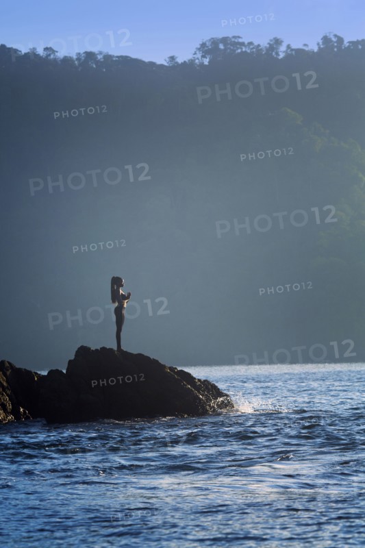 Mixed race woman standing on rock over ocean