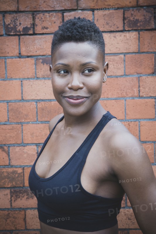 Black athlete smiling near brick wall