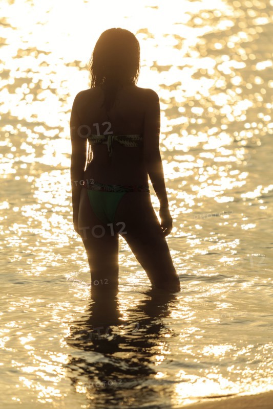 Silhouette of Mixed Race woman wading in ocean at sunset
