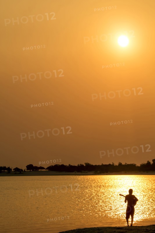 Silhouette of Caucasian man playing guitar at beach at sunset