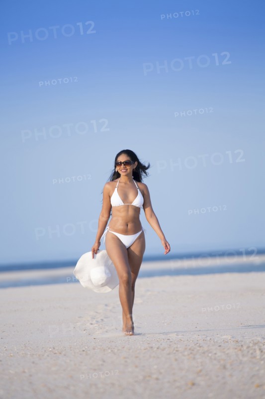 Smiling Mixed Race woman carrying sun hat on beach