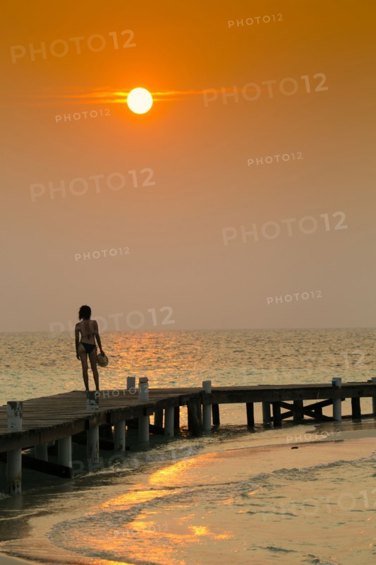 Mixed Race woman standing on ocean dock at sunset