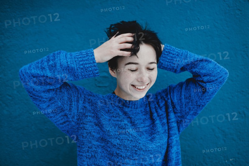Smiling Caucasian woman tousling hair near blue wall