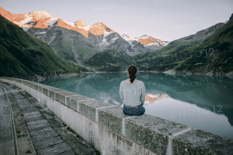 Caucasian woman sitting on wall at mountain lake