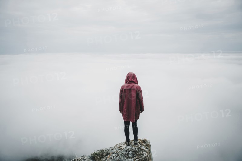 Distant Caucasian woman standing on rock watching fog on ocean