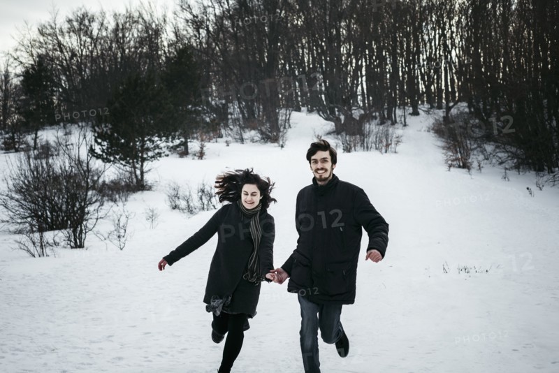Caucasian couple running from forest in winter