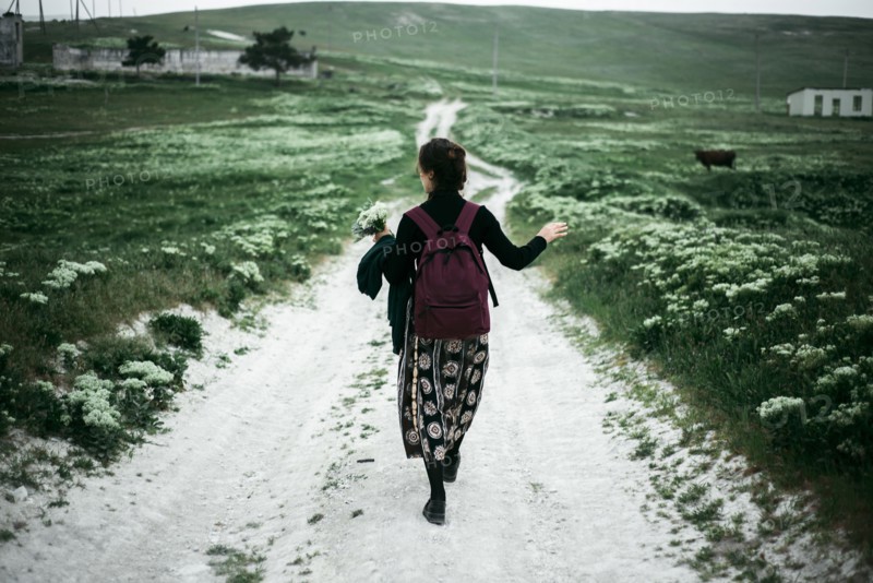 Caucasian woman walking on dirt road carrying wildflowers