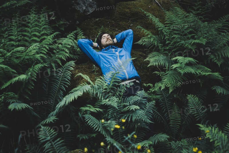 Caucasian man laying on rock in foliage