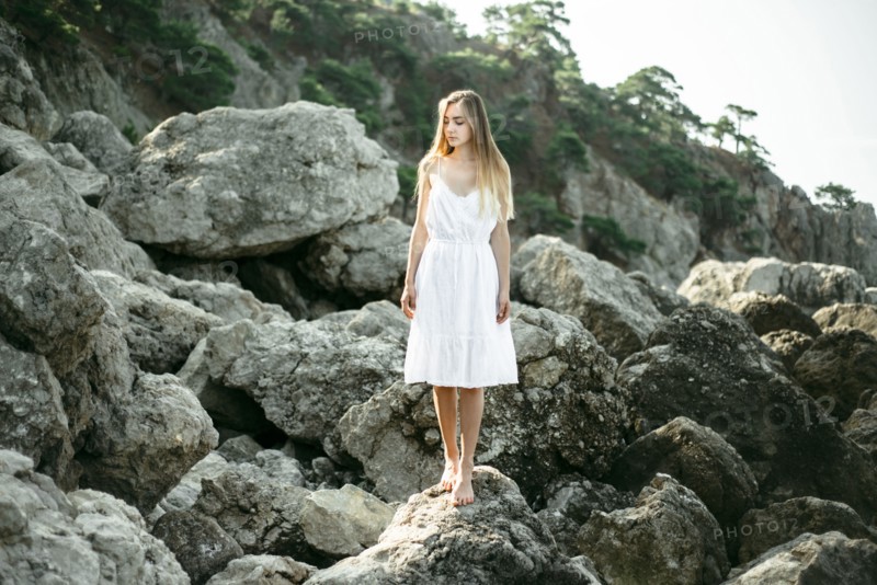 Caucasian woman wearing dress standing on rocks