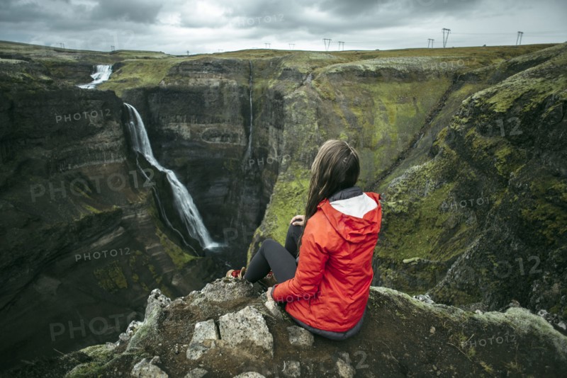 Caucasian woman sitting on cliff admiring waterfall