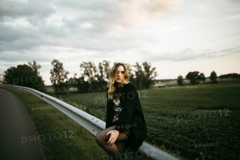 Caucasian woman sitting on guardrail near road