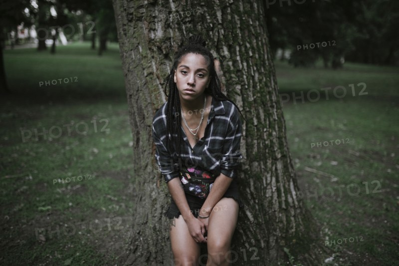 Portrait of serious African American woman leaning on tree