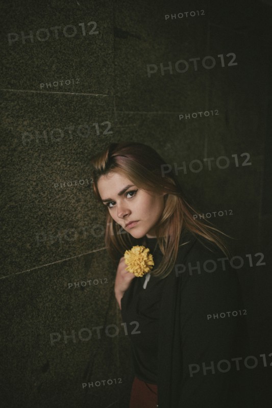 Serious Caucasian woman leaning on wall holding flower