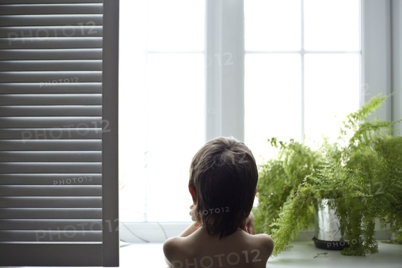Asian boy looking out bedroom window