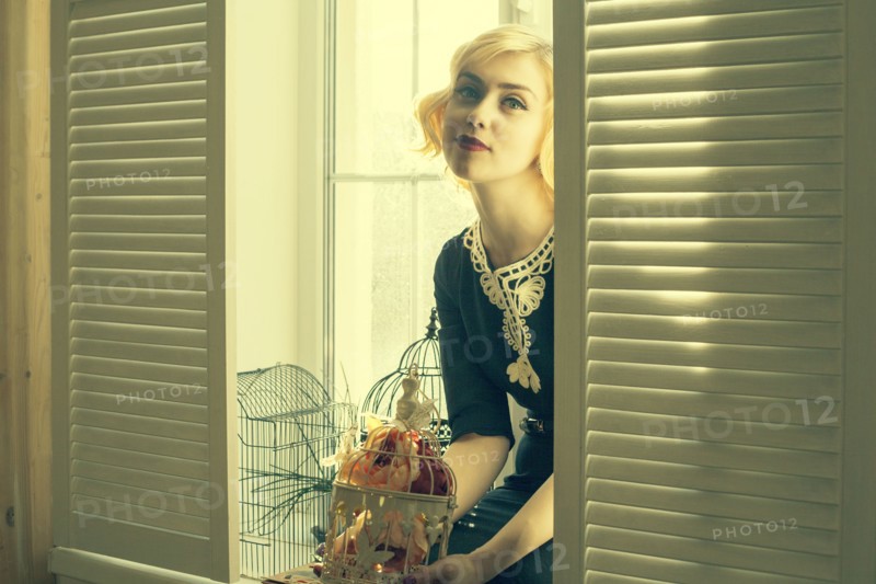 Caucasian woman holding birdcage in window