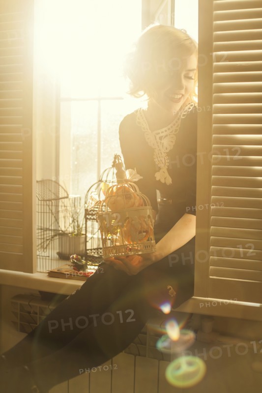Caucasian woman holding birdcage in window