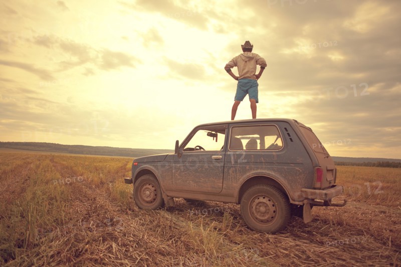 Mari man standing on car roof in rural field