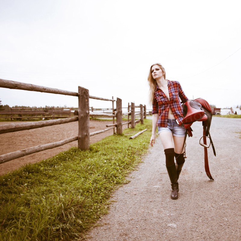 Caucasian woman carrying horse saddle on ranch