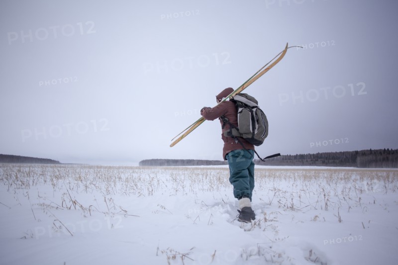 Mixed race man carrying skis in snowy field