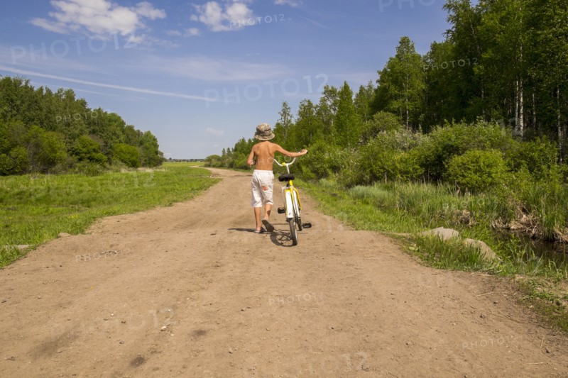 Mari boy walking bicycle on dirt path