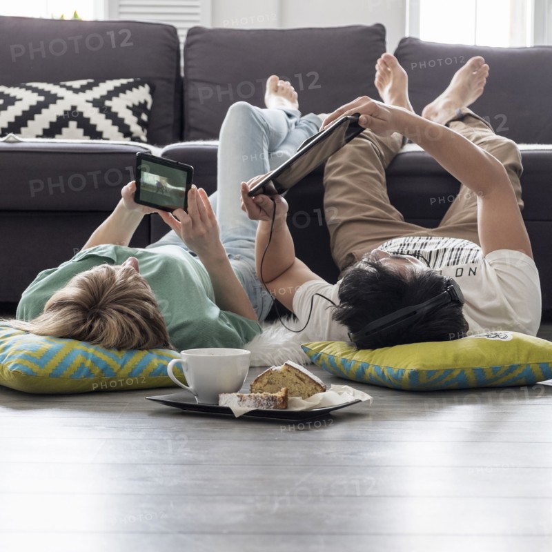 Caucasian couple using digital tablets on floor