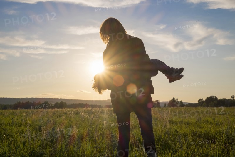 Woman carrying son in field at sunset
