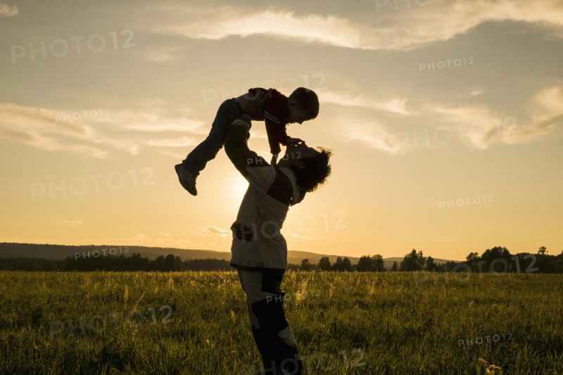 Mari man lifting son in field at sunset