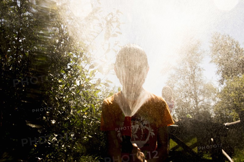 Back lit Mari boy spraying hose at face