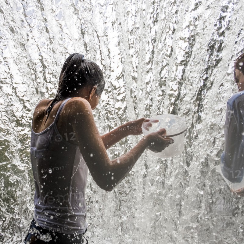 Caucasian mother and daughter holding containers in waterfall