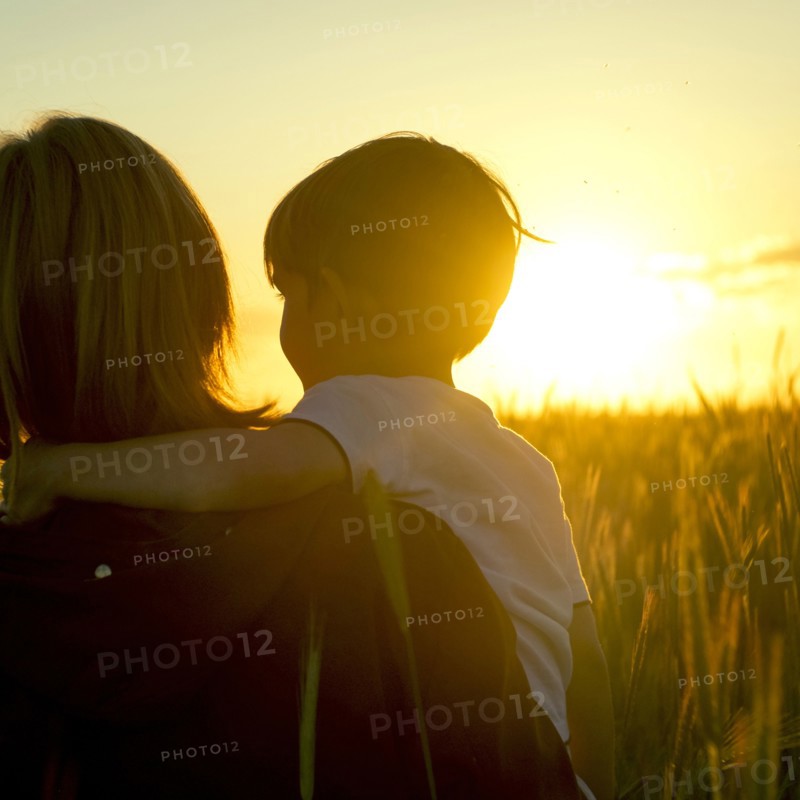 Mother carrying son in field of wheat at sunset