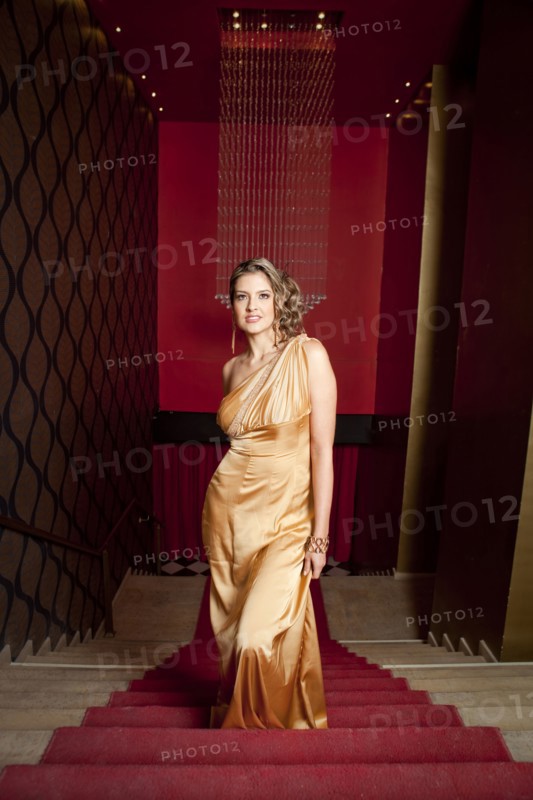 Glamorous Hispanic woman in evening gown standing on stairs