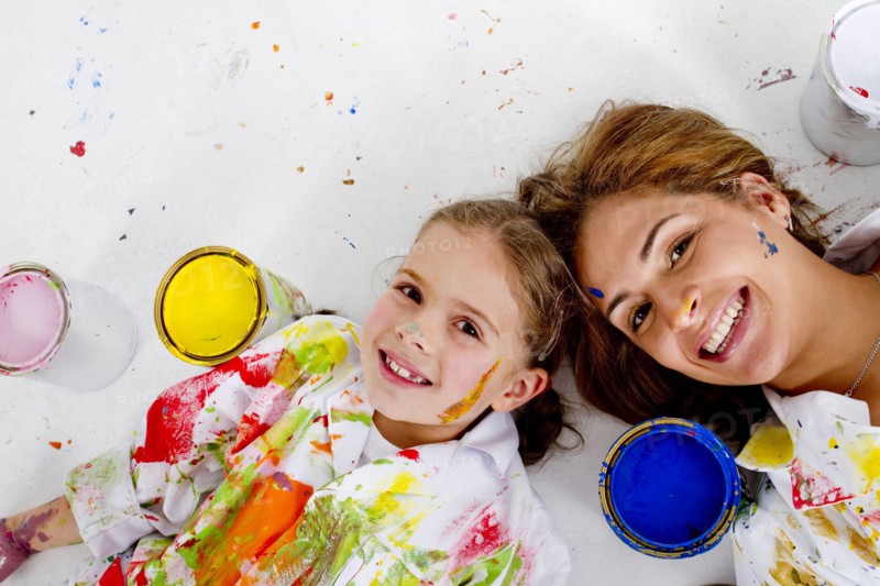 Hispanic mother and daughter covered in paint laying on floor