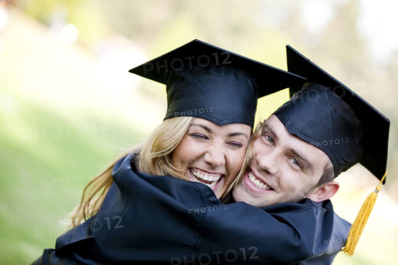 Graduating Hispanic couple in cap and gown hugging