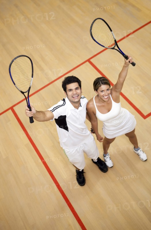 Hispanic couple raising squash racquets