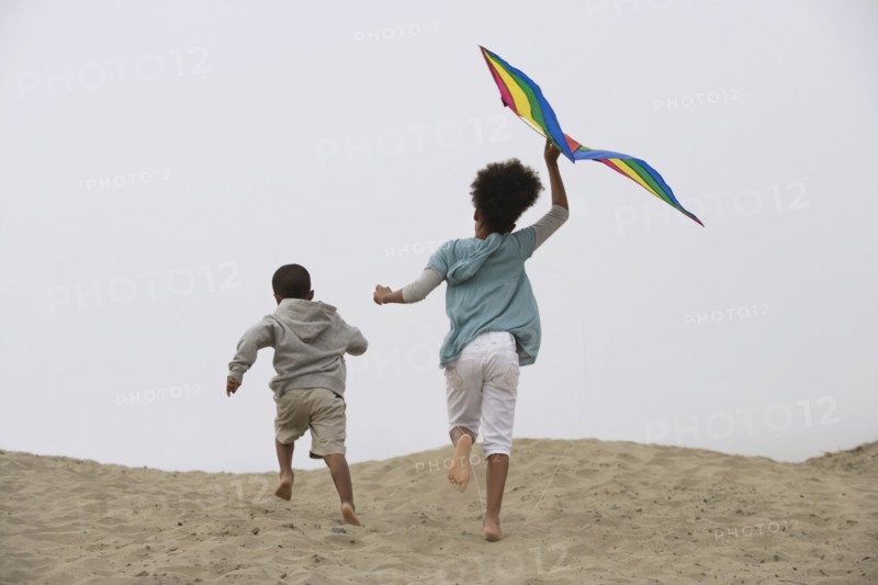 Mixed race children running on beach with kite
