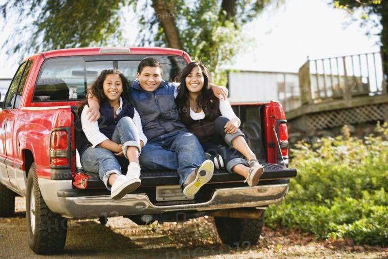 Hispanic siblings sitting in bed of truck