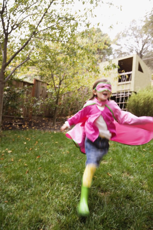 Middle Eastern girl wearing cape and mask running in backyard