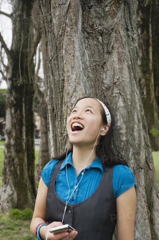 Chinese girl listening to headphones against tree