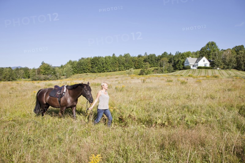 Caucasian woman leading horse through field