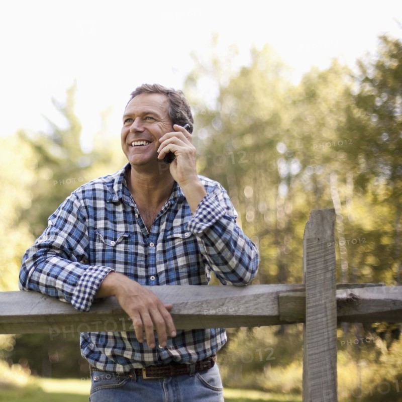 Caucasian man leaning on fence talking on cell phone