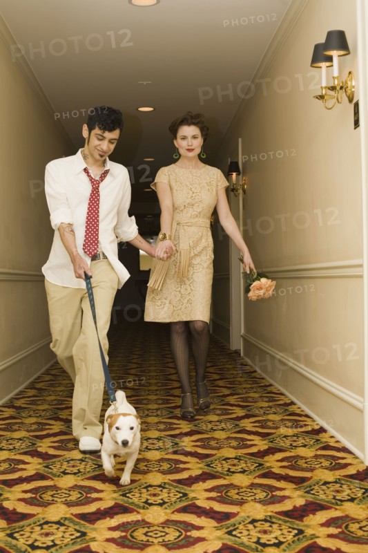 Young coupled dressed up walking down hotel hallway with dog