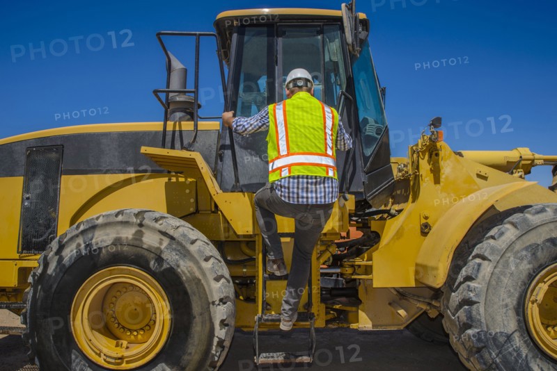 Caucasian construction worker climbing onto earth mover