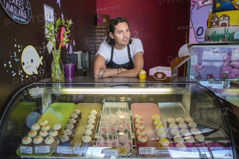 Hispanic business owner leaning on bakery display case