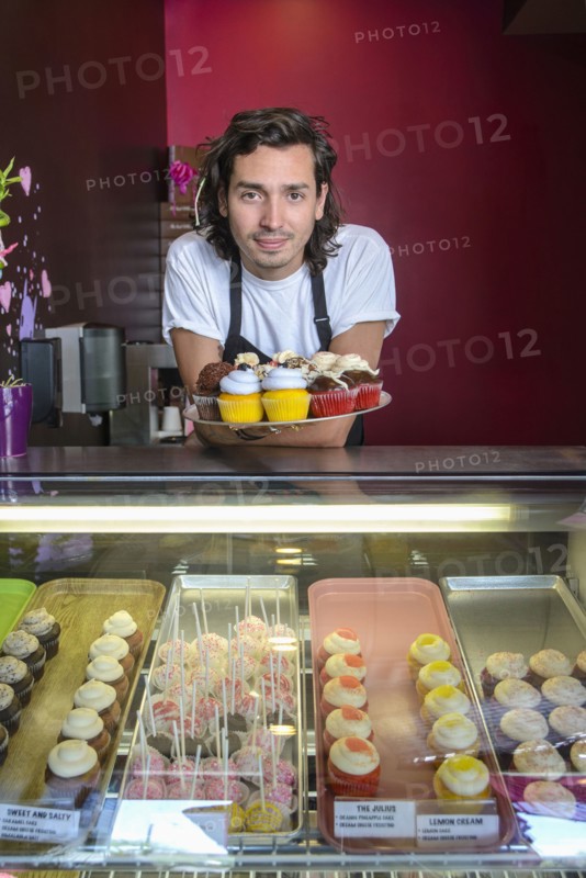 Hispanic business owner showing cupcakes bakery display case