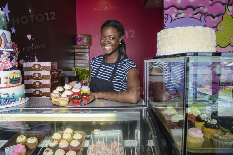Black business owner showing cupcakes at bakery display case