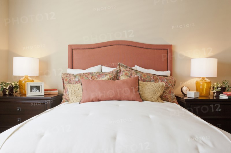 Arranged pillows on tidy bed with lit table lamps in the bedroom at home