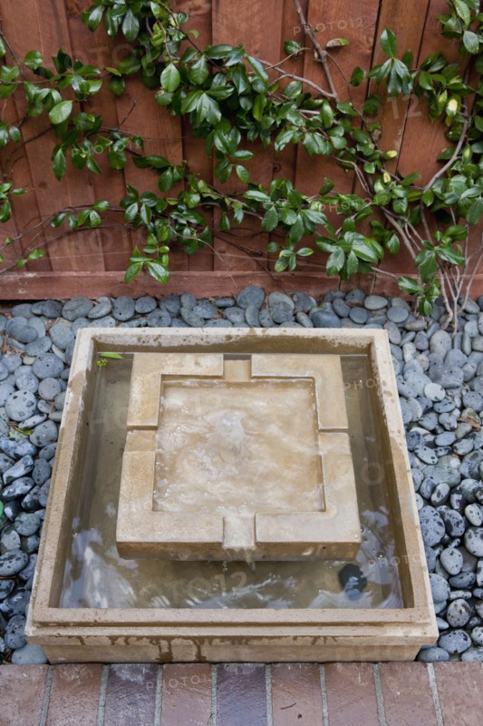 Square shaped fountain and pebbles outside house