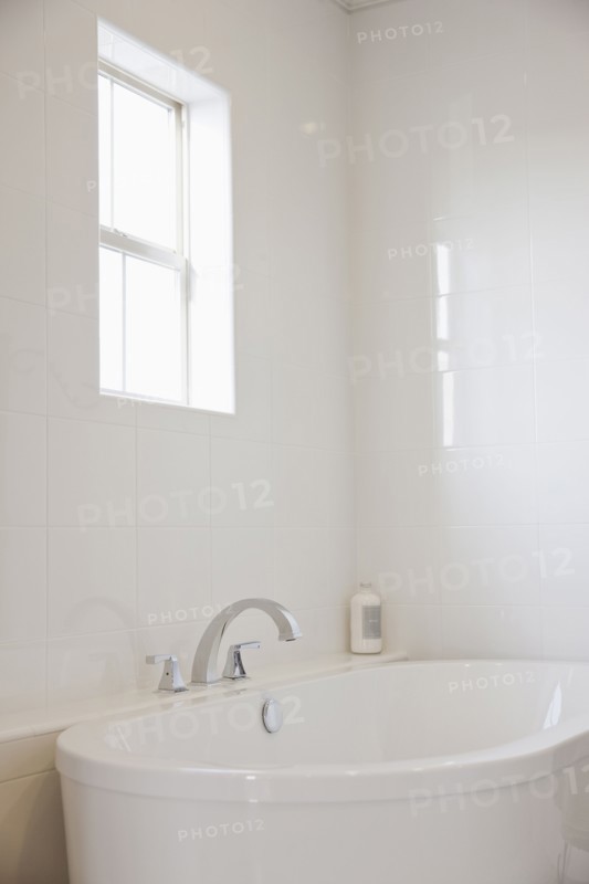 Close-up of a white bath with tiled wall and window in the bathroom