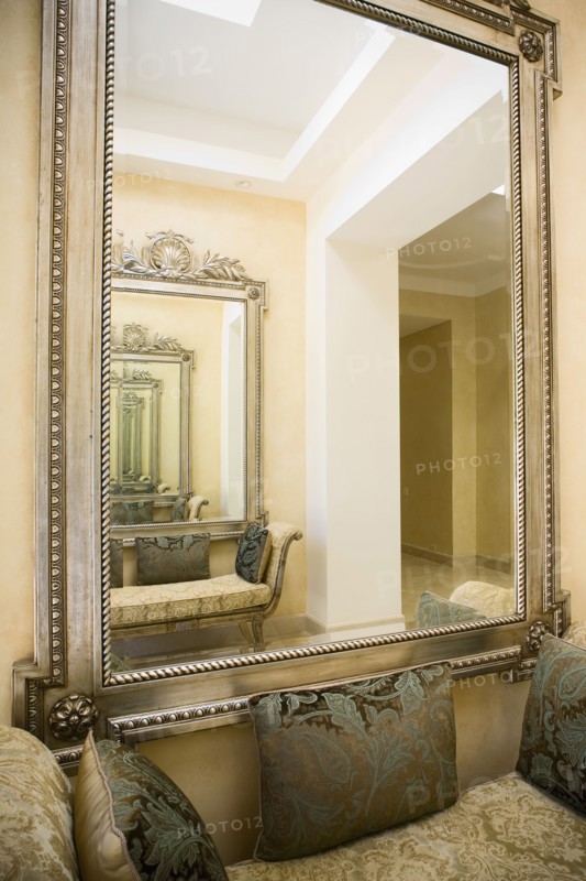 Detail of a large wall mirror over a loveseat with decorative pillows