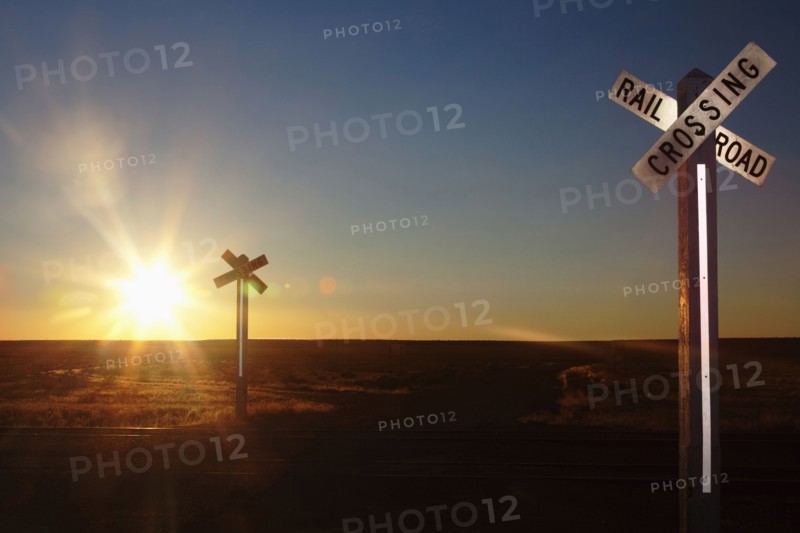 Railroad crossing sign on remote road at sunset